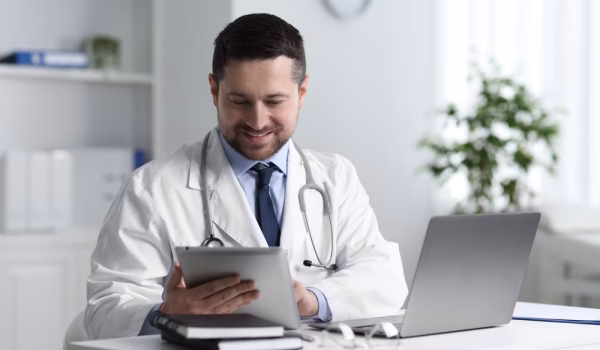 Smiling,Doctor,Having,Online,Consultation,Via,Tablet,At,Table,In